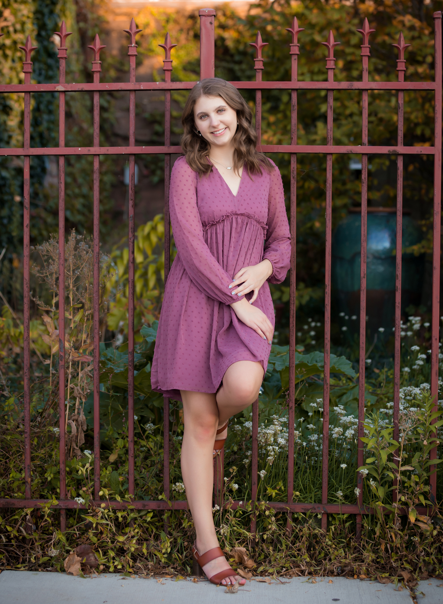 brown-haired-girl-in-raspberry-dress-leaning-against-fence