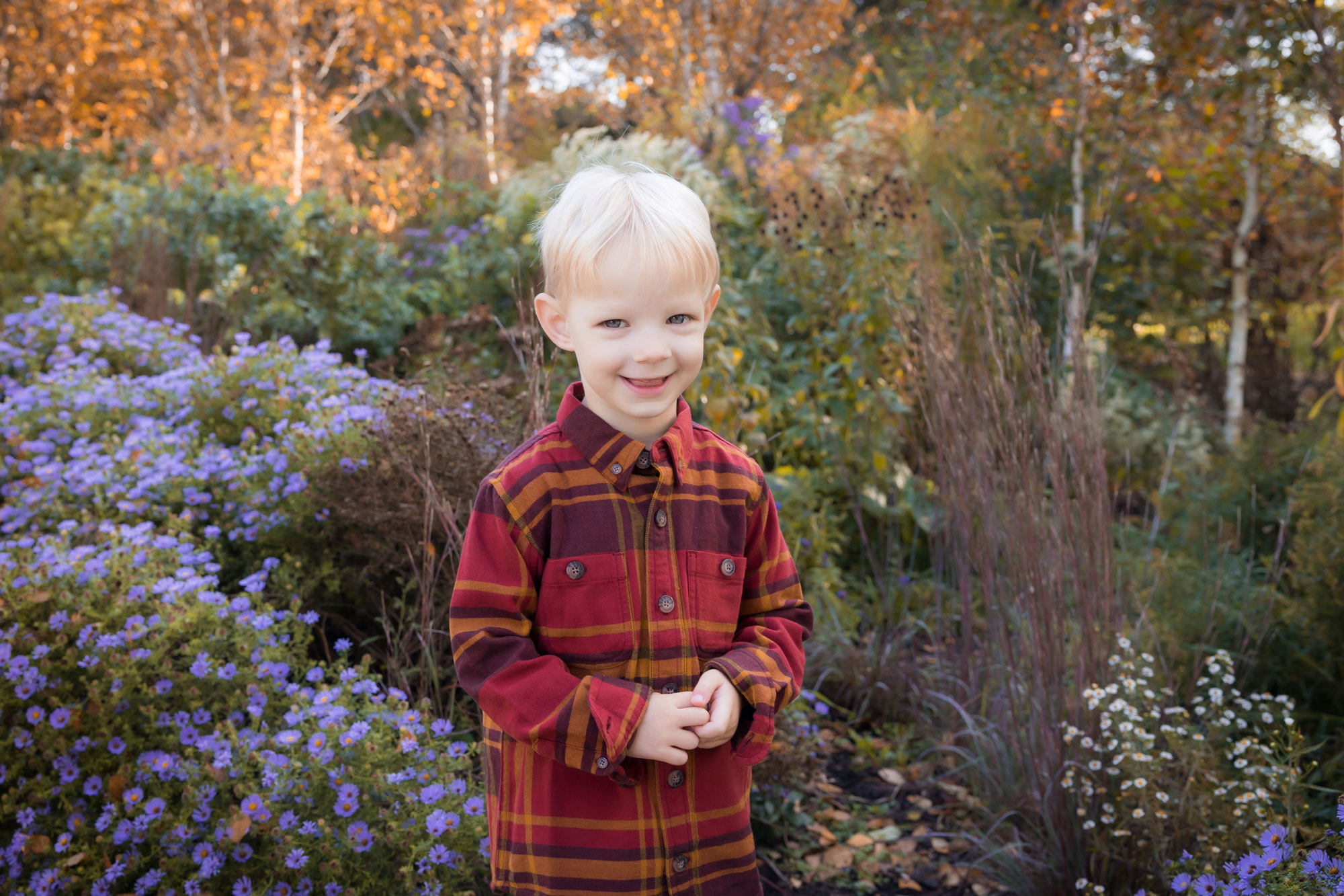 small blonde boy smiling at camera by flowers